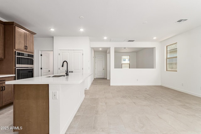 kitchen with a sink, double wall oven, light countertops, recessed lighting, and an island with sink