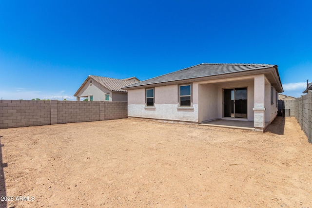 rear view of house featuring stucco siding, a tiled roof, a fenced backyard, and a patio area