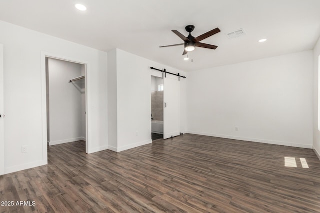 11474 N 79th Dr, Peoria, AZ 85345 - unfurnished bedroom featuring a barn door, dark wood-type flooring, recessed lighting, baseboards, and a spacious closet