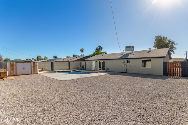 rear view of house with a fenced in pool, central air condition unit, a patio, and a storage unit