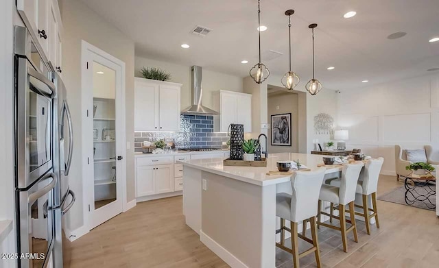 16342 W Jackson St, Goodyear, AZ 85338 - kitchen with wall chimney exhaust hood, light wood finished floors, decorative backsplash, white cabinets, and recessed lighting