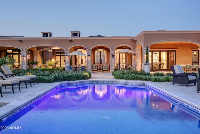 pool at dusk with french doors and a patio