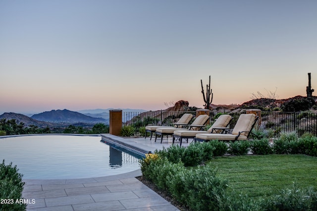 pool at dusk featuring a mountain view, a yard, and a patio