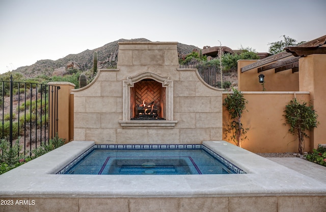 view of pool featuring an in ground hot tub, an outdoor fireplace, and a mountain view