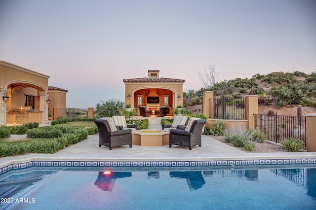 pool at dusk with a patio and an outdoor living space with a fireplace