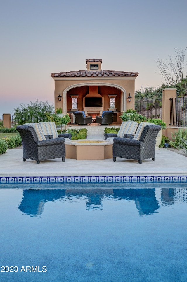 pool at dusk with an outdoor living space with a fireplace and a patio area