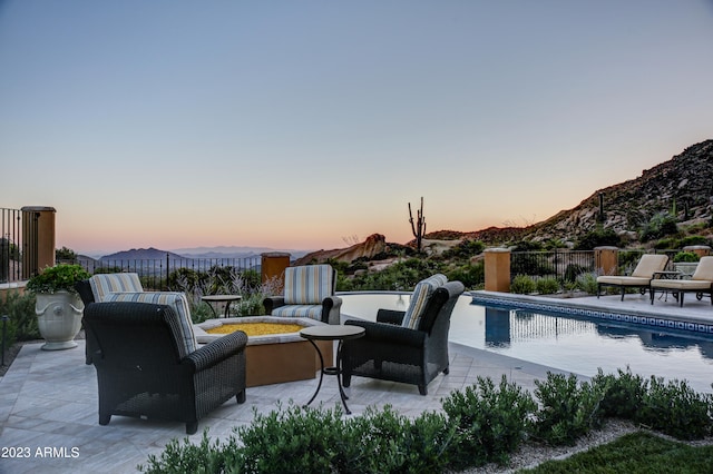 pool at dusk with a patio, an outdoor living space, and a mountain view