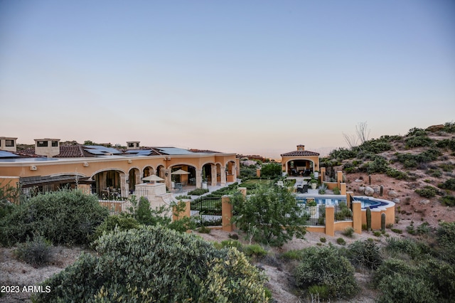 back house at dusk featuring a gazebo and a fenced in pool