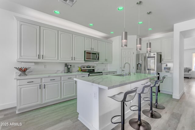 kitchen with visible vents, appliances with stainless steel finishes, a sink, hanging light fixtures, and light wood finished floors