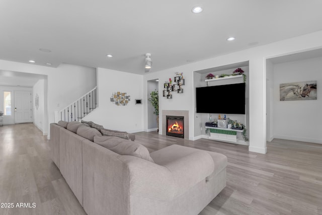 living area with a glass covered fireplace, recessed lighting, stairway, and light wood-style floors