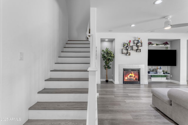 staircase featuring a tiled fireplace, baseboards, recessed lighting, and wood finished floors
