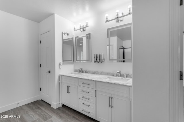 full bathroom featuring a sink, baseboards, double vanity, and wood finished floors