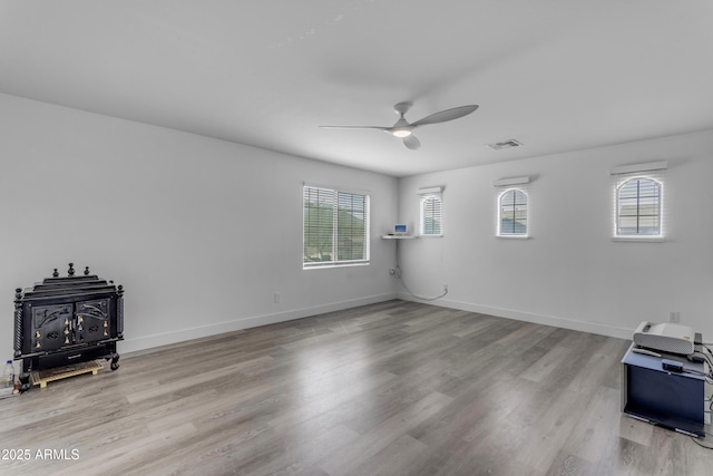 unfurnished living room with baseboards, a ceiling fan, a wood stove, visible vents, and wood finished floors