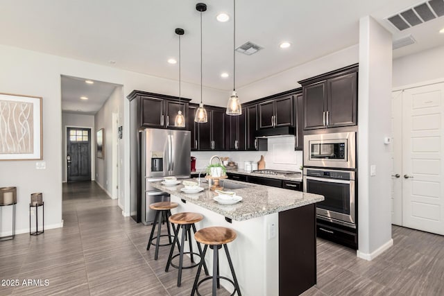 kitchen with appliances with stainless steel finishes, an island with sink, visible vents, and decorative light fixtures