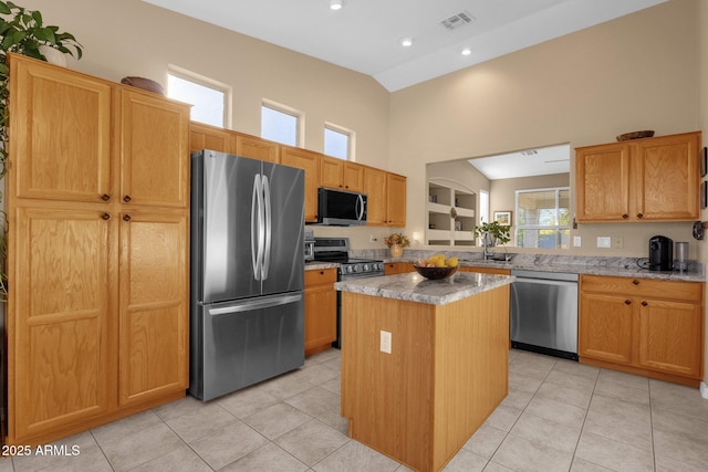 kitchen featuring a kitchen island, light stone countertops, appliances with stainless steel finishes, and light tile patterned floors