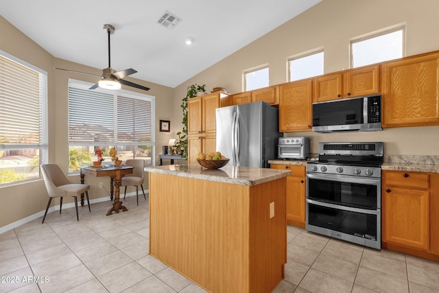 kitchen featuring lofted ceiling, a center island, light tile patterned floors, stainless steel appliances, and light stone countertops