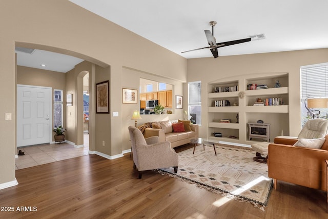 living room with vaulted ceiling, built in features, ceiling fan, and light wood-type flooring