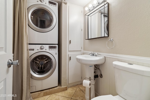 bathroom featuring stacked washer and clothes dryer, tile patterned floors, and toilet