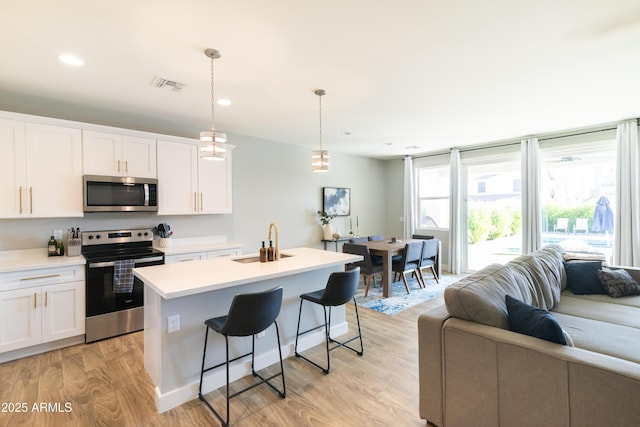 kitchen featuring sink, a kitchen island with sink, stainless steel appliances, white cabinets, and decorative light fixtures