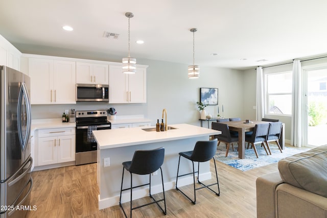 kitchen featuring sink, appliances with stainless steel finishes, a kitchen island with sink, white cabinets, and decorative light fixtures