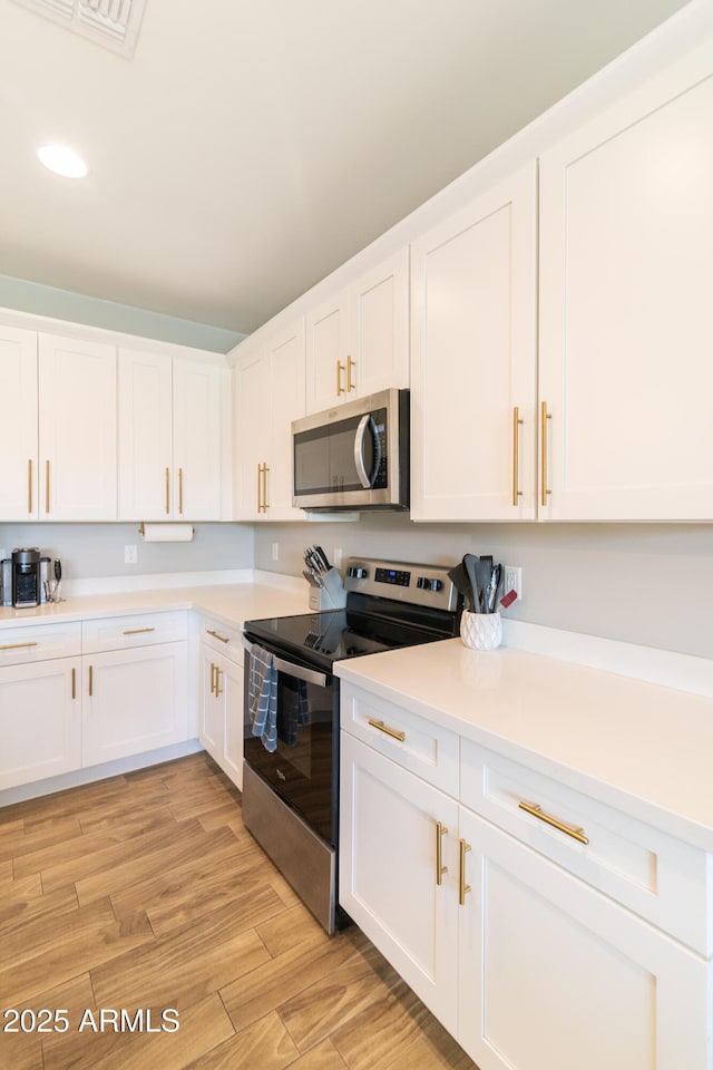 kitchen with appliances with stainless steel finishes, white cabinets, and light hardwood / wood-style floors