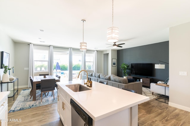 kitchen with pendant lighting, sink, dishwasher, white cabinetry, and a kitchen island with sink