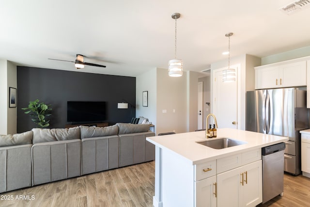 kitchen with sink, appliances with stainless steel finishes, white cabinetry, hanging light fixtures, and a center island with sink