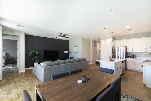 dining space featuring ceiling fan, sink, and light wood-type flooring