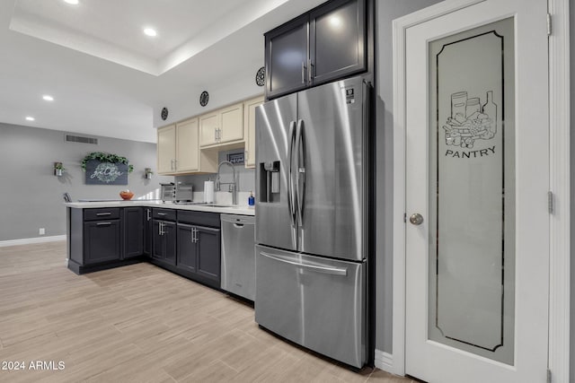 kitchen with gray cabinetry, sink, stainless steel appliances, light hardwood / wood-style flooring, and a tray ceiling