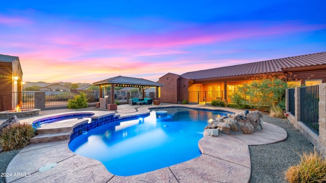 pool at dusk featuring an in ground hot tub, a gazebo, a patio area, and a fire pit