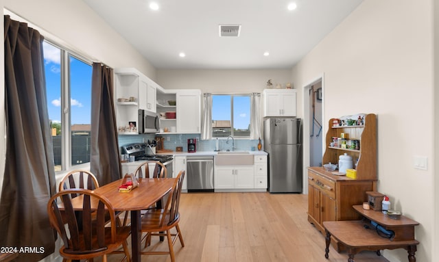 kitchen with sink, tasteful backsplash, light wood-type flooring, appliances with stainless steel finishes, and white cabinets