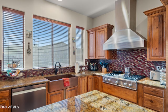 kitchen featuring sink, light stone counters, appliances with stainless steel finishes, wall chimney range hood, and backsplash