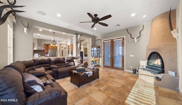 living room featuring ceiling fan with notable chandelier, a fireplace, and french doors