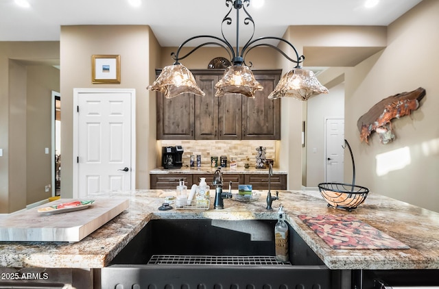 kitchen featuring tasteful backsplash, light stone countertops, dark brown cabinets, and an island with sink