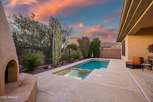 pool at dusk with an in ground hot tub and a patio