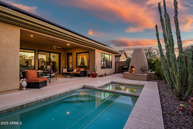 pool at dusk with an outdoor living space with a fireplace, ceiling fan, a patio area, and an in ground hot tub