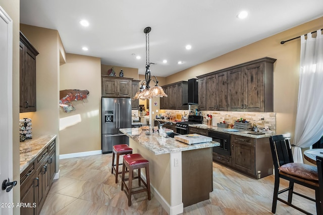 kitchen featuring black microwave, wall chimney exhaust hood, stainless steel fridge with ice dispenser, range with gas cooktop, and an island with sink