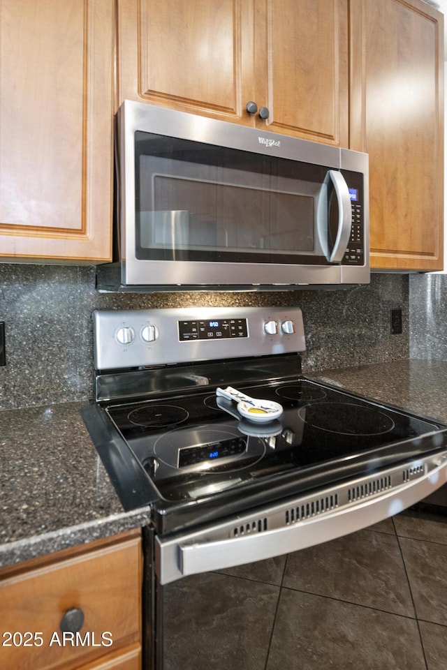 kitchen featuring stainless steel appliances, tile patterned flooring, dark stone countertops, and decorative backsplash