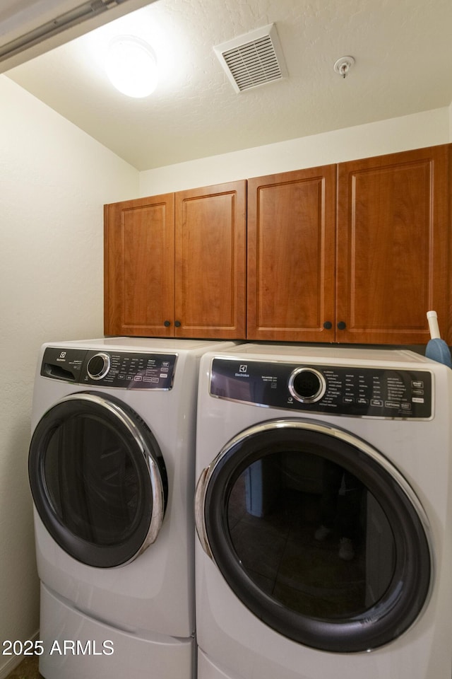 clothes washing area featuring cabinets and washer and clothes dryer