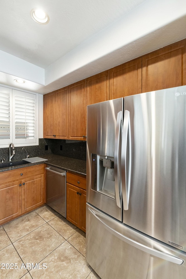 kitchen featuring stainless steel appliances, light tile patterned flooring, sink, and dark stone counters