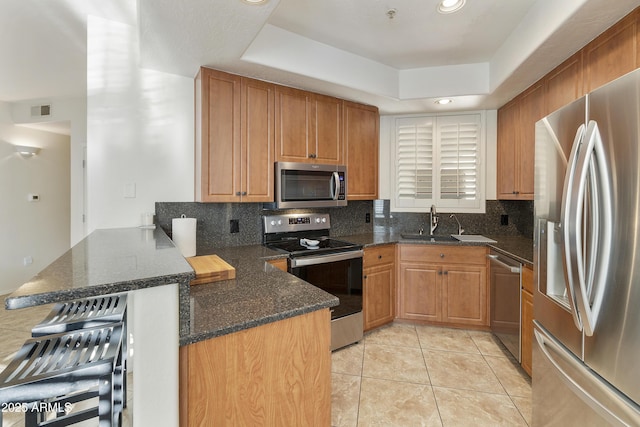 kitchen with tasteful backsplash, appliances with stainless steel finishes, a tray ceiling, and kitchen peninsula