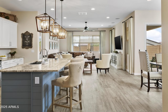 kitchen with light stone counters, a sink, visible vents, white cabinets, and light wood-type flooring