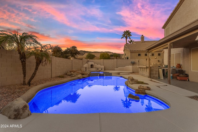 pool at dusk featuring a patio area, an in ground hot tub, and exterior kitchen