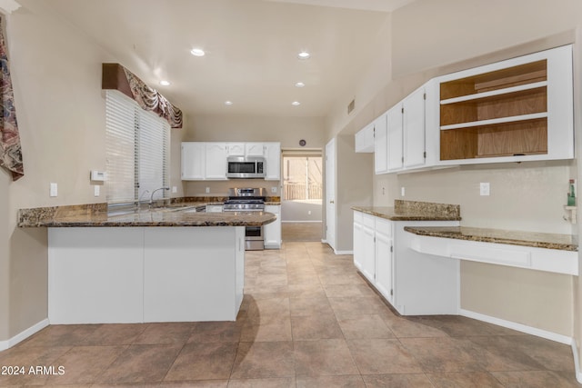 kitchen with sink, stainless steel appliances, kitchen peninsula, dark stone countertops, and white cabinets