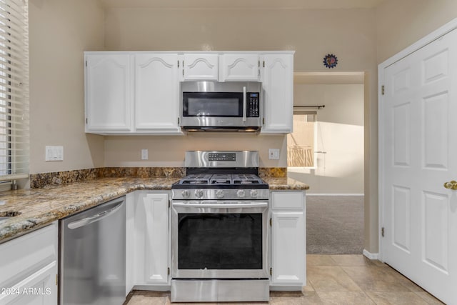 kitchen featuring stone counters, white cabinets, stainless steel appliances, and light carpet