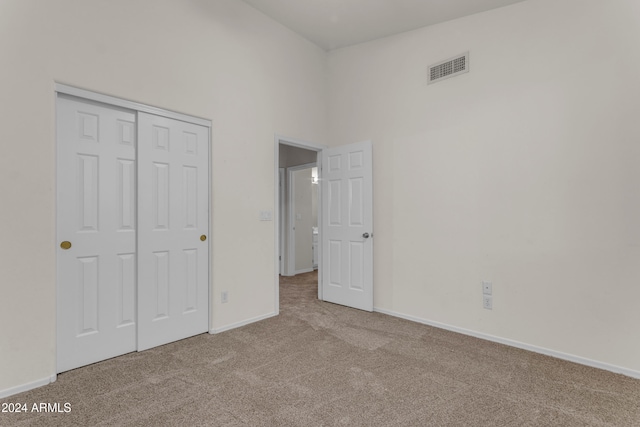 unfurnished bedroom with a closet, light colored carpet, and a high ceiling