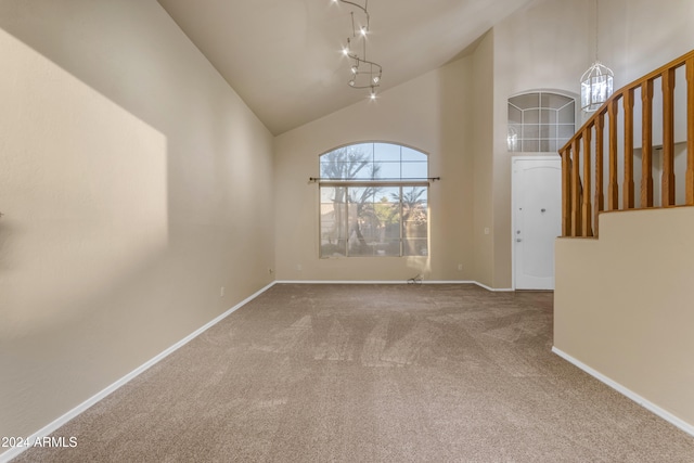 carpeted empty room with high vaulted ceiling, track lighting, and a notable chandelier