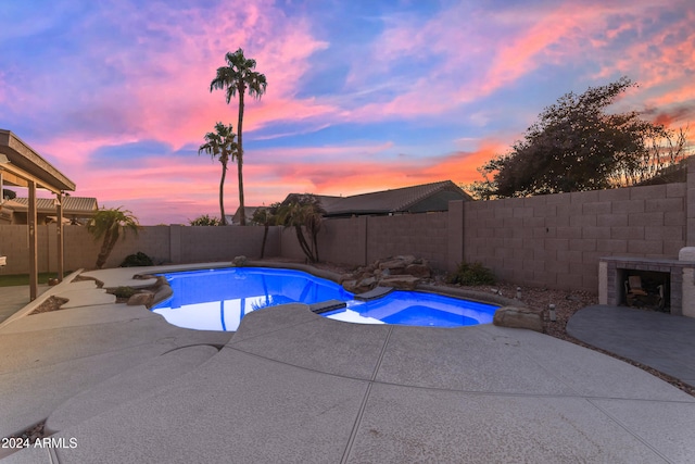 pool at dusk with a patio and exterior fireplace