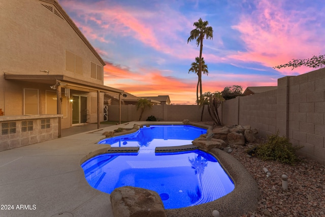 pool at dusk with an in ground hot tub and a patio