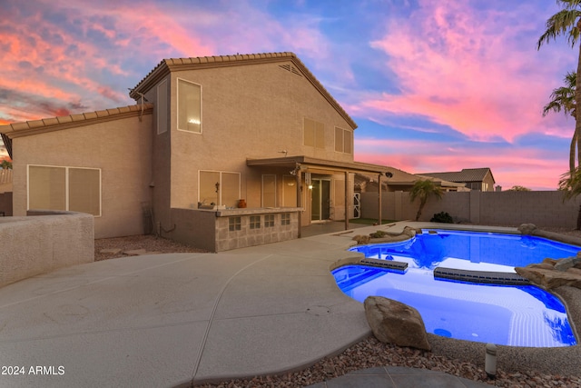 pool at dusk with a patio area, an in ground hot tub, and an outdoor kitchen